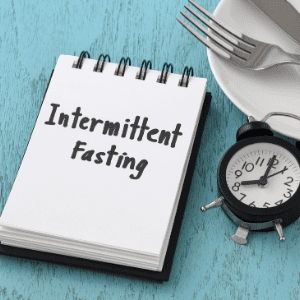 intermittent fasting written on a pad next to a clock and knife and fork